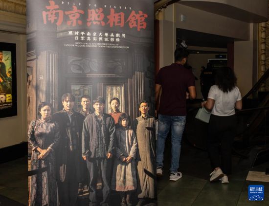 8月15日，在美國紐約市一家電影院，觀眾經過電影《南京照相館》的海報。新華社發（周煥新攝）